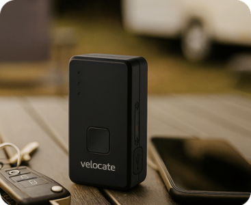 Ein vc mini 2 GPS-Ger&auml;t steht auf einem Campingtisch, daneben liegen ein Autoschl&uuml;ssel und ein ausgeschaltetes Smartphone. Im Hintergrund ist ein verschmutztes Freizeitfahrzeug zu sehen.